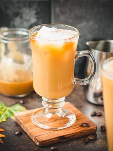 Tall coffee glass filled with iced caramel latte, with homemade caramel milk. Placed on wooden coaster.