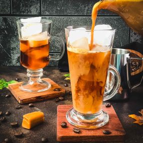 Tall, narrow coffee-filled glass, gets filled with ice-cold homemade caramel milk.