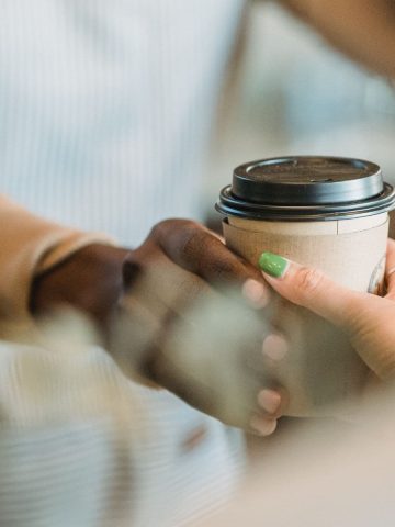 Two hands passing each other a cup of coffee.