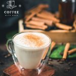 Gorgous cinnamon dolce latte, dusted with ground cinnamon. Placed on wooden coaster with cinnamon sticks in the background.