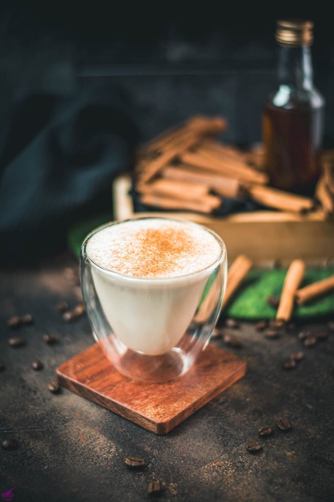 Gorgous cinnamon dolce latte, dusted with ground cinnamon. Placed on wooden coaster with cinnamon sticks in the background.