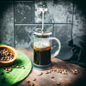 French press filled with cold water and ground coffee next to a bowl of coffee beans - an easy way to make cold brew coffee!