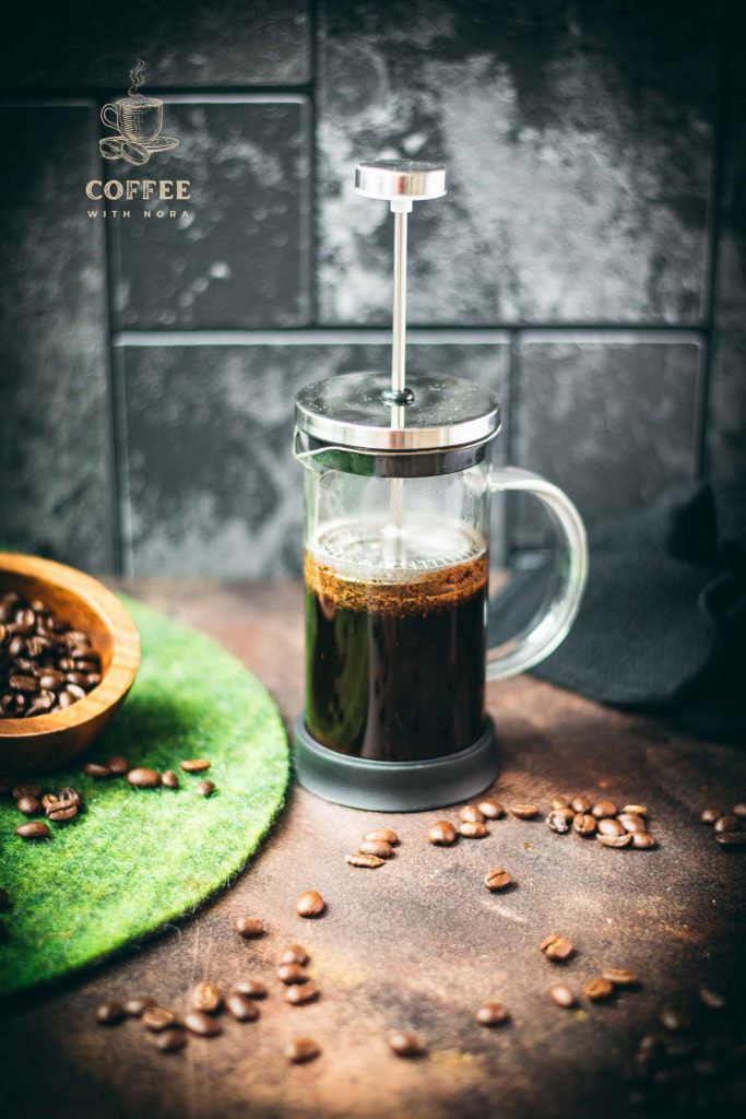 French press filled with cold water and ground coffee next to a bowl of coffee beans - an easy way to make cold brew coffee!