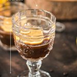 Two beautiful glasses filled with coffee and a slice of lemon stand on a dark background.