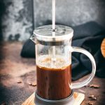 French press coffee maker filled with coffee on a wooden coaster.