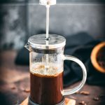 French press coffee maker filled with coffee on a wooden coaster.