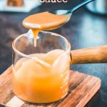 Spoon with homemade caramel sauce hovering over glass jar filled with caramel sauce.