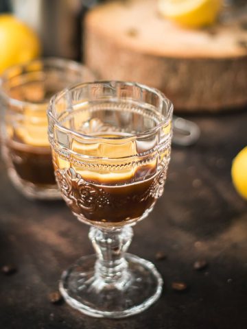 Two beautiful glasses filled with coffee and a slice of lemon stand on a dark background.