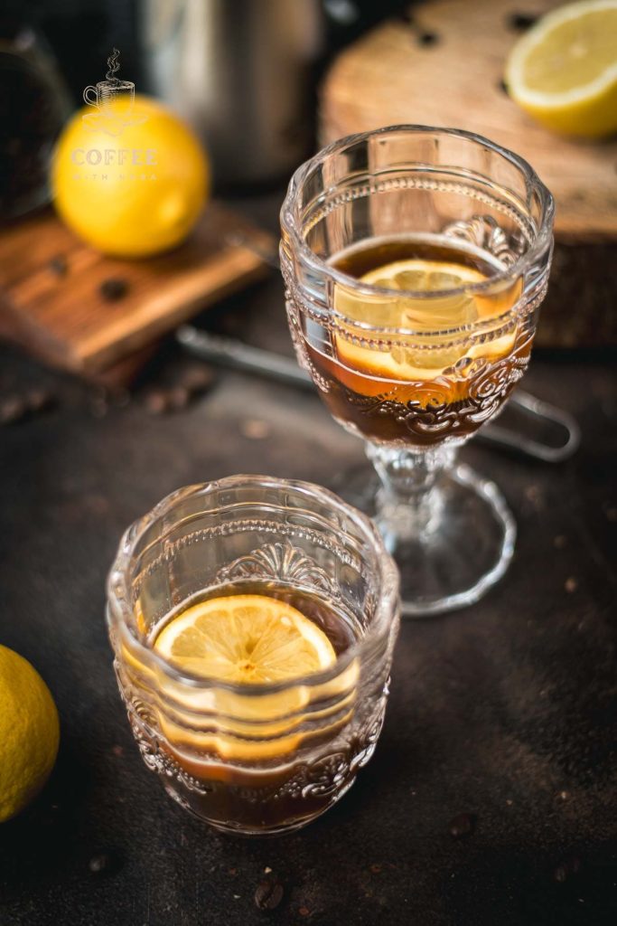 Two beautiful glasses filled with coffee and a slice of lemon stand on a dark background.