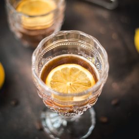 One beautiful glass filled with coffee and a slice of lemon stands on a dark background.