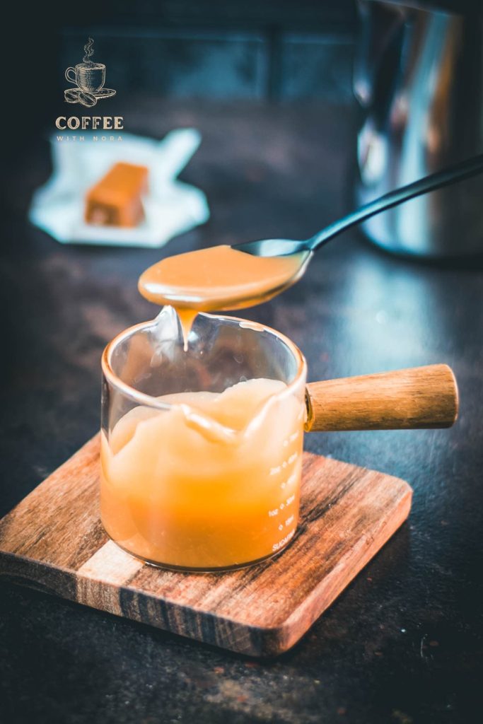 Spoon with homemade caramel sauce hovering over glass jar filled with caramel sauce.