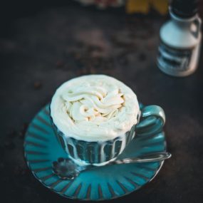 Blue coffee mug with coffee and maple syrup whipped cream topping. A little overflowing.