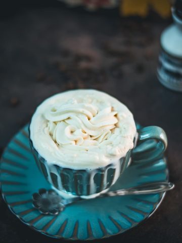 Blue coffee mug with coffee and maple syrup whipped cream topping. A little overflowing.