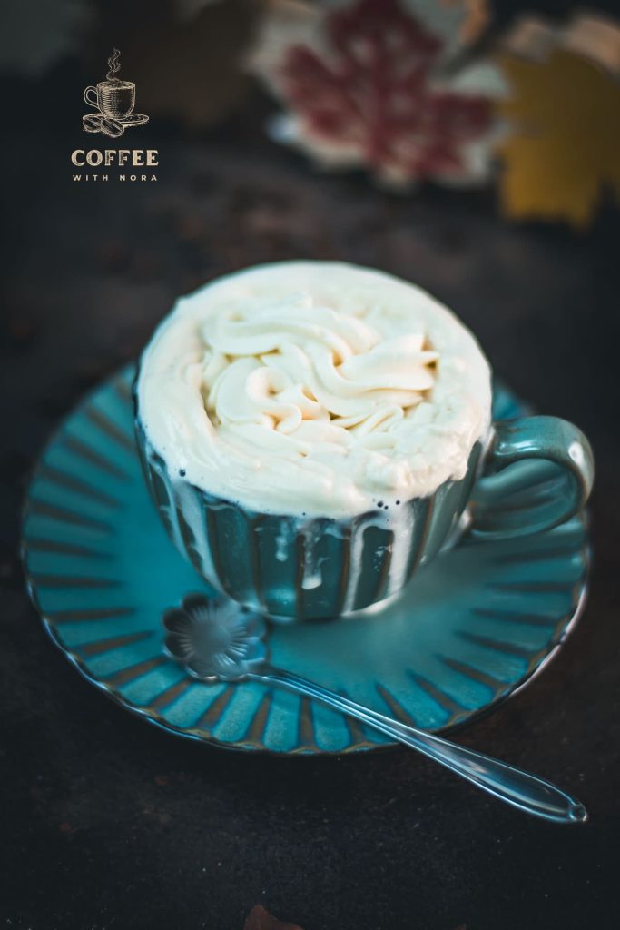 Blue coffee mug with coffee and maple syrup whipped cream topping. A little overflowing.