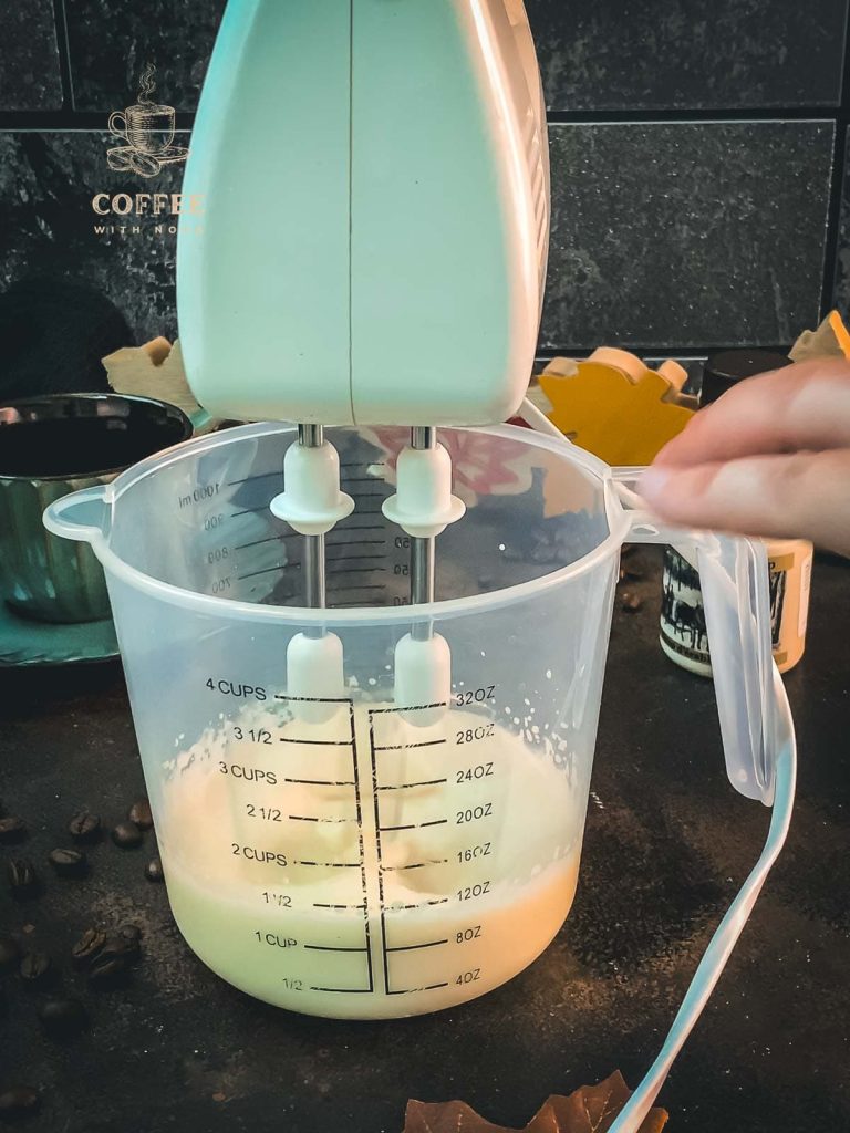 Elextric mixer beats heavy cream in measuring cup.