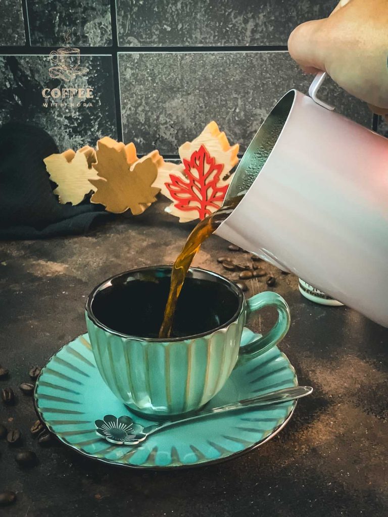 Coffee is poured into a coffee mug using a metal pitcher.