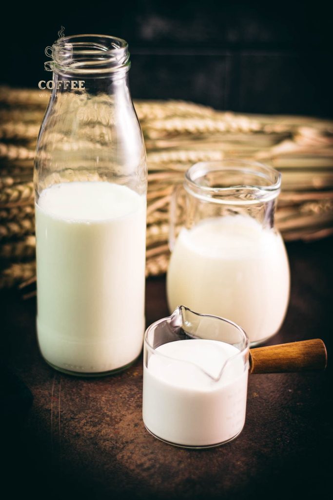 A bottle, a jug and a small container filled with different types of milk. Placed on a dark ground.