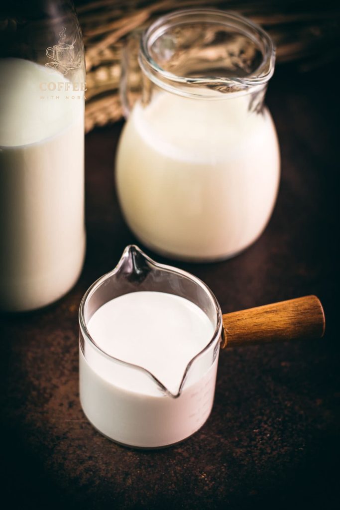 A bottle, a jug and a small container filled with different types of milk. Placed on a dark ground.