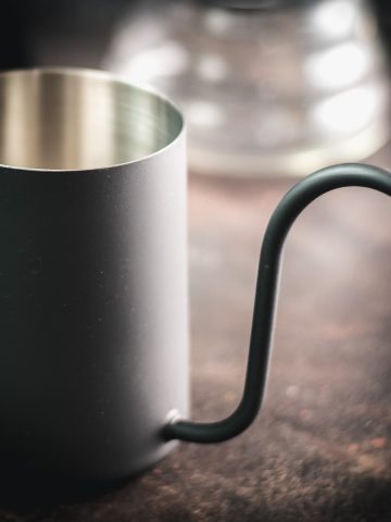 Gorgeous black gooseneck kettle on dark ground placed next to a V60 Pour Over Kit.