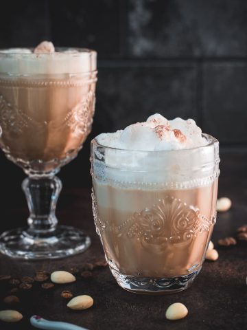 Gorgeous almond milk lattes, in gorgeous glasses, placed on dark floor.