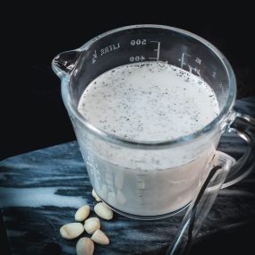 Glass jug filled with almond vanilla milk, placed on marble plate.