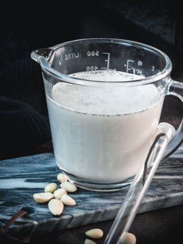 Glass jug filled with almond vanilla milk, placed on marble plate.