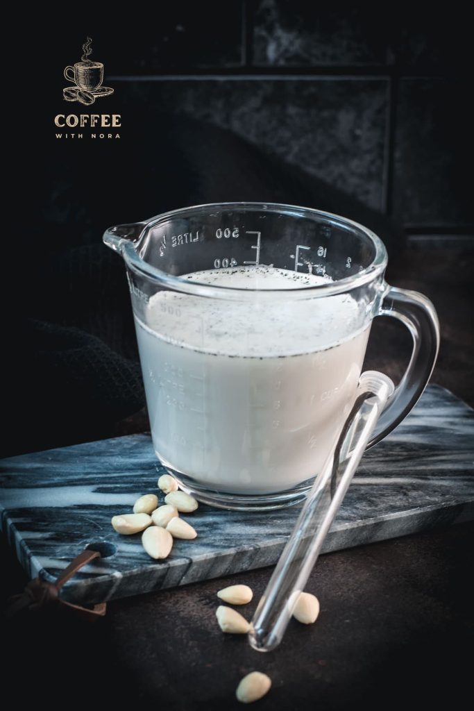 Glass jug filled with almond vanilla milk, placed on marble plate.