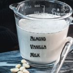 Glass jug filled with almond vanilla milk, placed on marble plate.