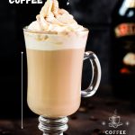 Gorgeous glass filled with scrumptious Bailey's coffee, topped with whipped cream and dusted with cocoa. Placed on dark ground in front of an Salted Baileys Caramel bottle.