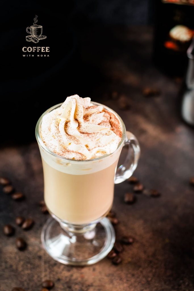 Gorgeous glass filled with scrumptious Bailey's coffee, topped with whipped cream and dusted with cocoa. Placed on dark ground in front of an Salted Baileys Caramel bottle.