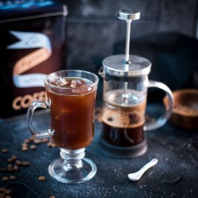 Cute glass filled with French press iced coffee placed next to French press.