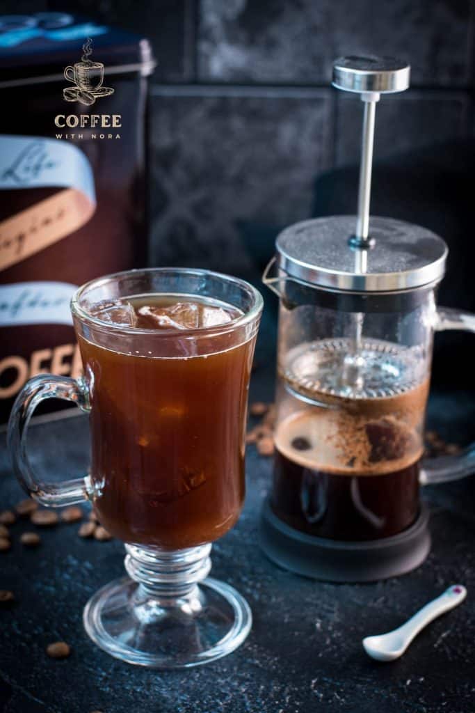 Cute glass filled with French press iced coffee placed next to French press.