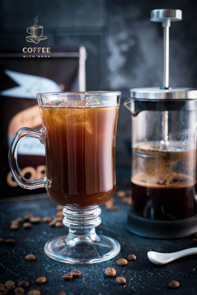 Cute glass filled with French press iced coffee placed next to French press.