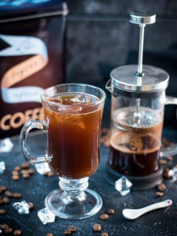 Cute glass filled with French press iced coffee placed next to French press.