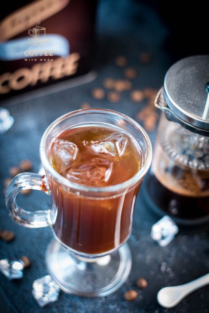 Cute glass filled with French press iced coffee placed next to French press.