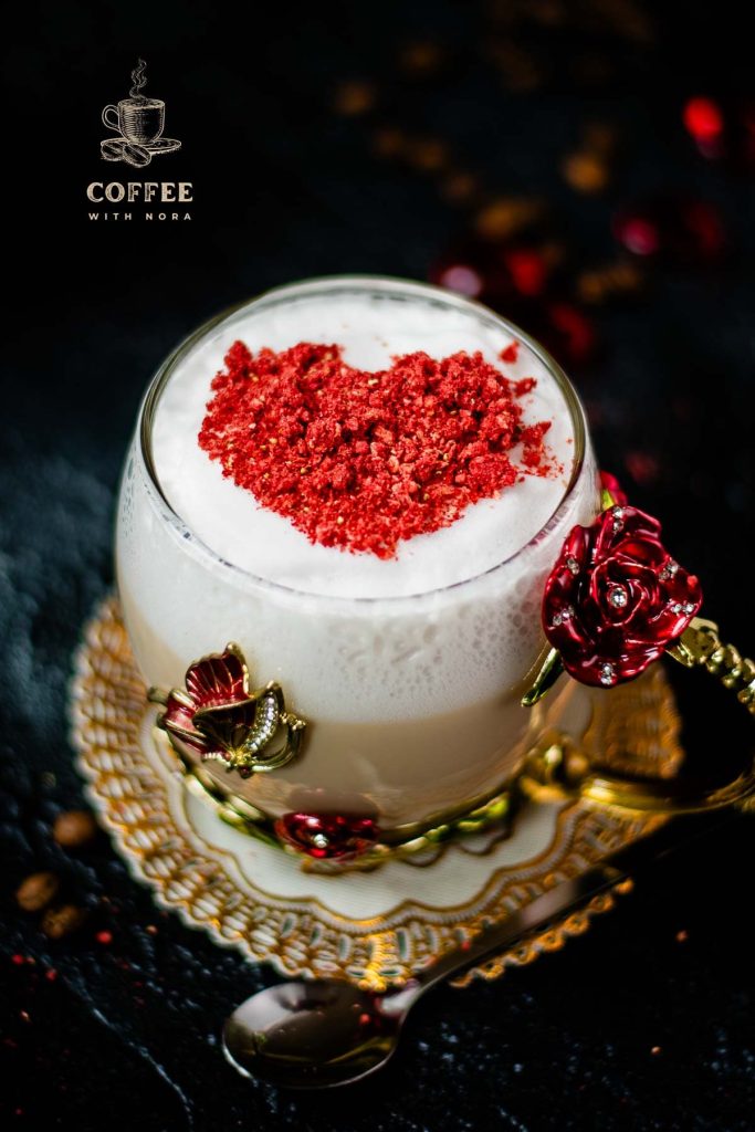 Beautiful coffee glass decorated with a red and gold butterfly and flowers. Filled with delicious strawberry latte and topped with heart-shaped freeze-dried strawberry powder. Placed on dark ground.