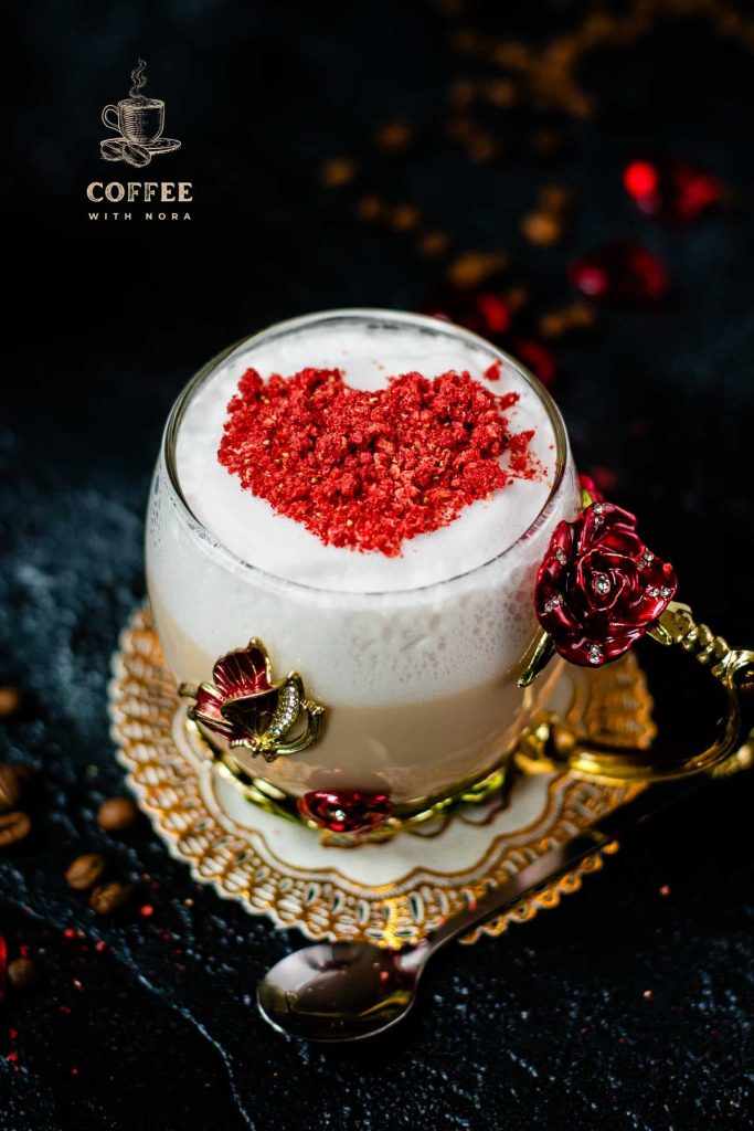 Beautiful coffee glass decorated with a red and gold butterfly and flowers. Filled with delicious strawberry latte and topped with heart-shaped freeze-dried strawberry powder. Placed on dark ground.