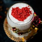 Beautiful coffee glass decorated with a red and gold butterfly and flowers. Filled with delicious strawberry latte and topped with heart-shaped freeze-dried strawberry powder. Placed on dark ground.