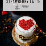 Beautiful coffee glass decorated with a red and gold butterfly and flowers. Filled with delicious strawberry latte and topped with heart-shaped freeze-dried strawberry powder. Placed on dark ground.