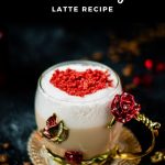 Beautiful coffee glass decorated with a red and gold butterfly and flowers. Filled with delicious strawberry latte and topped with heart-shaped freeze-dried strawberry powder. Placed on dark ground.