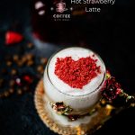 Beautiful coffee glass decorated with a red and gold butterfly and flowers. Filled with delicious strawberry latte and topped with heart-shaped freeze-dried strawberry powder. Placed on dark ground.