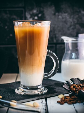 Gorgeous glass filled with ice cold plant based vanilla iced coffee. Placed on black slate plate.