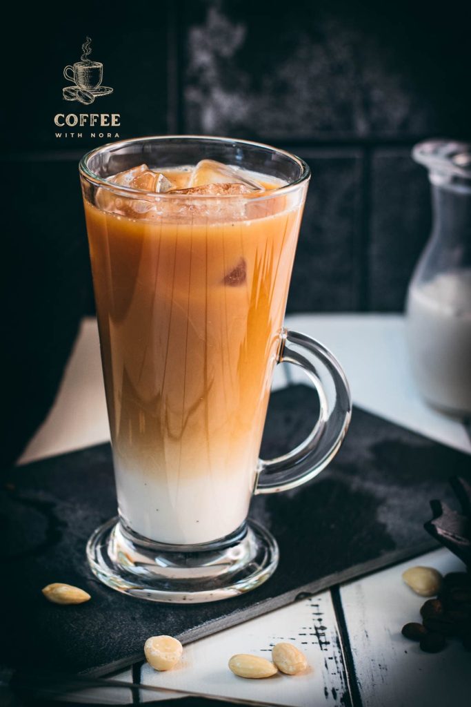 Gorgeous glass filled with ice cold plant based vanilla iced coffee. Placed on black slate plate.