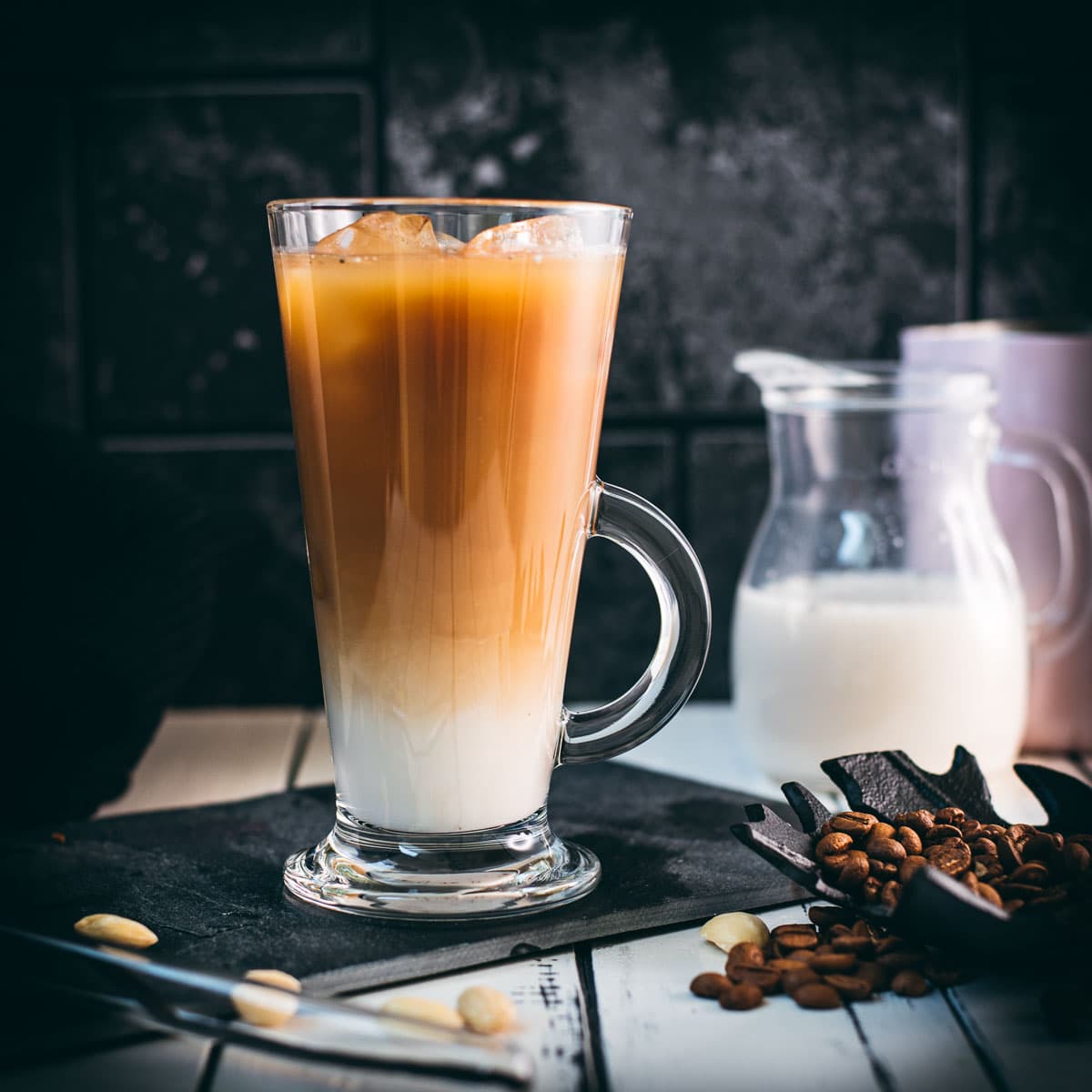 Gorgeous glass filled with ice cold plant based vanilla iced coffee. Placed on black slate plate.