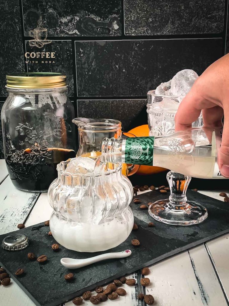 Pouring ginger beer into a glass filled with cubed ice.