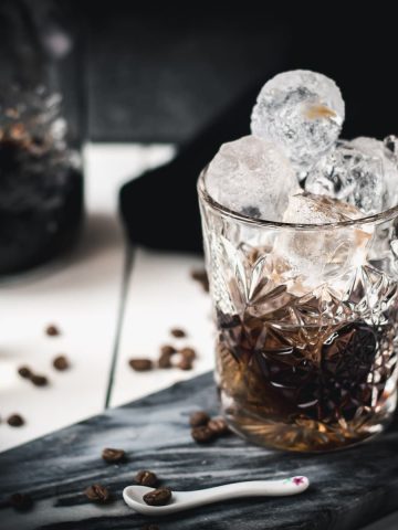 Gorgeous cold brew black Russian served in a rocks glass and placed on a marbled plate.