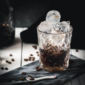 Gorgeous cold brew black Russian served in a rocks glass and placed on a marbled plate.