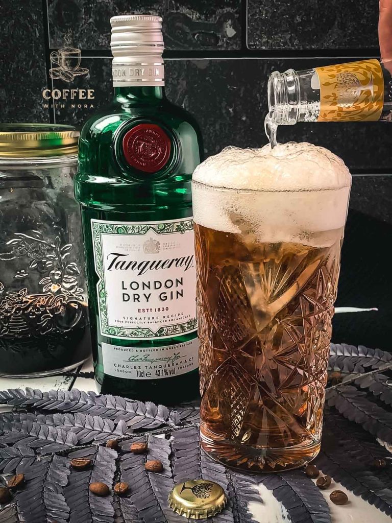 Pouring the tonic water into the highball glass filled with gin and cold brew.