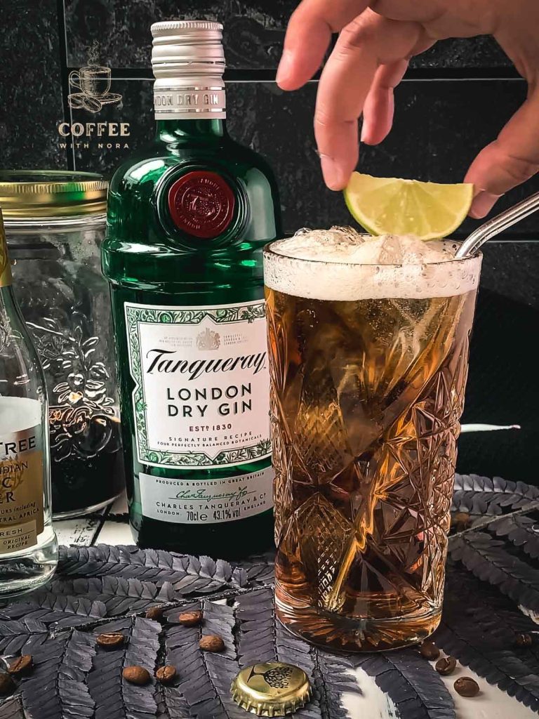 Hand placing a lime slice on top of the cold brew gin tonic.