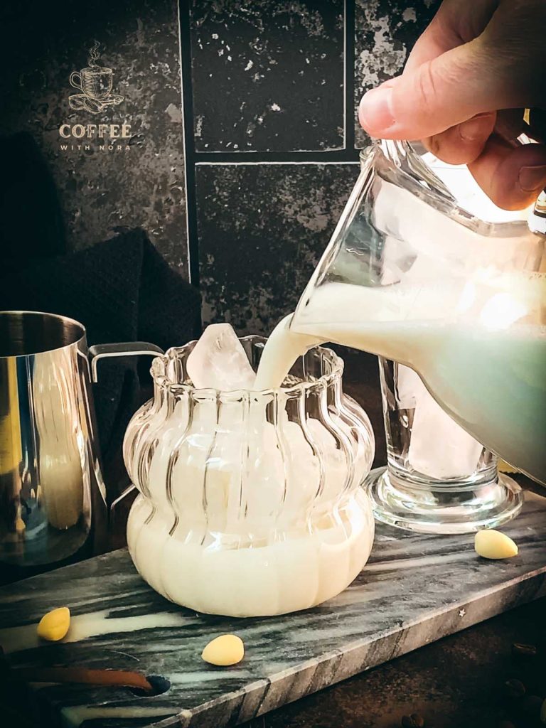 Pouring almond milk to the glass filled with cubed ice.